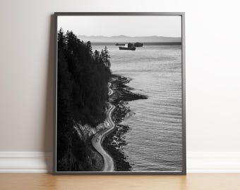 May include: Black and white framed photograph showing a coastal road snaking along a cliff edge, with the sea to the right. The road curves, and the cliff is covered in trees. Ships are visible in the distance.