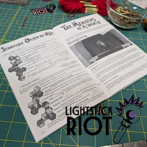 Puede incluir: Libro abierto con texto sobre una serie de historias y tesoros, con el texto "LIGHTSTICK RIOT" en la parte inferior. El libro est&aacute; sobre una esterilla de corte verde, con hilo rojo y llaves en el fondo.
