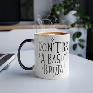 Könnte beinhalten: Eine weiße Keramiktasse mit schwarzem Henkel. Die Tasse hat ein schwarzes Design mit dem Text "Don't be a basic bruja" und Sternen drumherum.