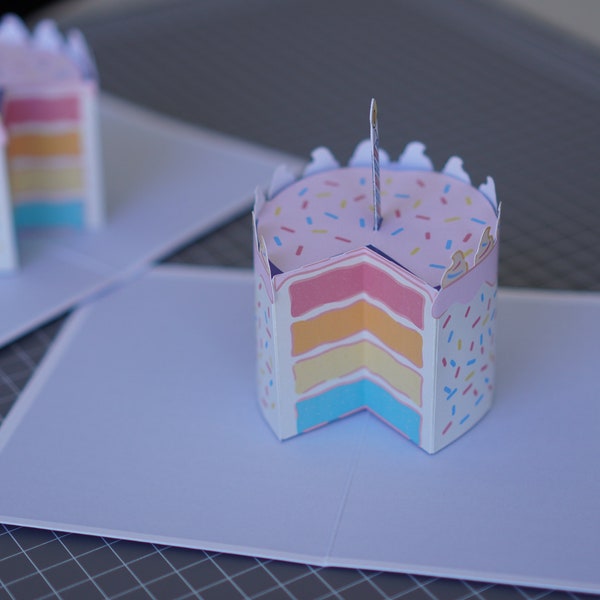 Carte popup de gâteau d'anniversaire - un gâteau d'anniversaire arc-en-ciel avec un morceau coupé