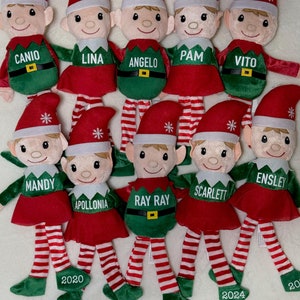 May include: Ten plush elf dolls with red and green outfits and personalized names. Each elf has a red hat with a white snowflake and a white number on the bottom of their green shoes. The names on the elves are Canio, Lina, Angelo, Pam, Vito, Mandy, Apollonia, Ray Ray, Scarlett, and Ensley.