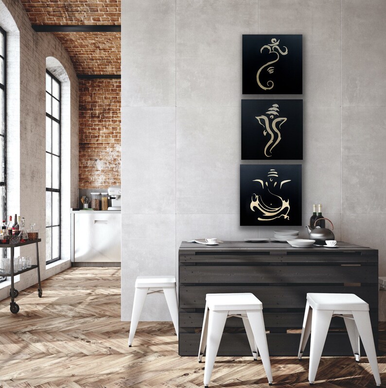 Pu&ograve; includere: Tre tele quadrate nere con contorni dorati che rappresentano la divinit&agrave; ind&ugrave; Ganesha in diverse pose. Le tele sono appese a un muro grigio in una cucina moderna.