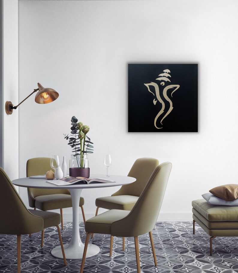 Pu&ograve; includere: Un'opera d'arte murale su tela nera con un contorno dorato della divinit&agrave; ind&ugrave; Ganesha. L'opera &egrave; esposta in una sala da pranzo moderna con un tavolo bianco e sedie verdi.