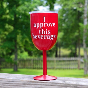 May include: A red wine glass with a white inscription that reads "I approve this beverage."