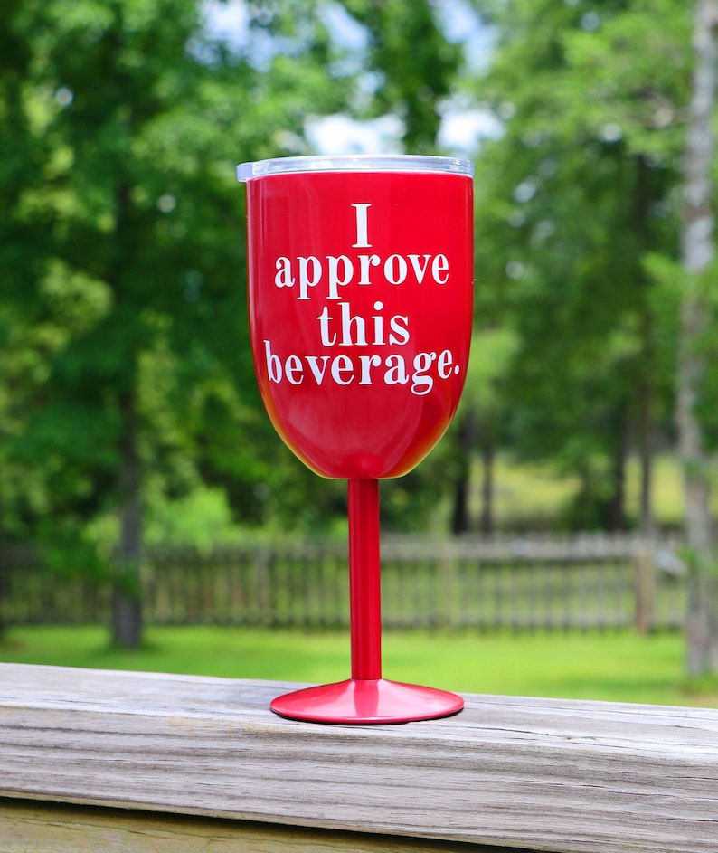 May include: A red wine glass with a white inscription that reads "I approve this beverage."