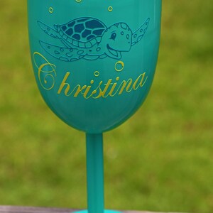May include: A turquoise blue stainless steel wine tumbler with a lid and a sea turtle design. The tumbler has the name "Christina" written on it in yellow.