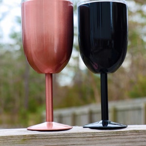 May include: Two stainless steel wine tumblers, one rose gold and one black, with a clear lid. The tumblers are on a wooden surface.