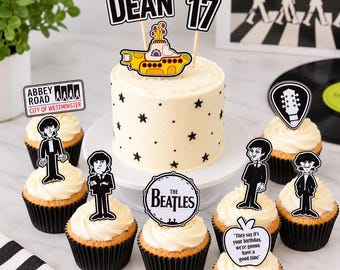 May include: A white frosted cake and cupcakes decorated with Beatles-themed paper toppers. The cake features a yellow submarine, the name DEAN, and the number 17. Cupcakes include illustrations of band members, Abbey Road signage, and text.
