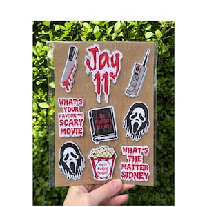May include: A sheet of horror movie-themed stickers on a brown card. Designs include a bloody knife, a retro mobile phone, and the Ghostface mask. Text includes "Jay 11", "What's Your Favourite Scary Movie", and "What's the Matter Sidney".
