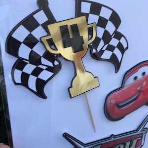 May include: Cake toppers featuring a gold trophy with the number 4, checkered flags, and a red race car. The word "Joey" is also visible in a racing-themed font. These decorations are perfect for a birthday party.