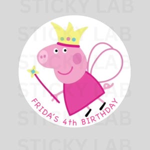 Puede incluir: Una pegatina redonda con un cerdo de dibujos animados que lleva una corona y alas de hada, sosteniendo una varita mágica. El cerdo es rosa con una cara sonriente. El texto en la pegatina dice "FRIDA'S 4th BIRTHDAY". El fondo es blanco.
