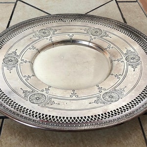 May include: A silver serving tray with a decorative, ornate design. The tray has a raised rim and a centre well.