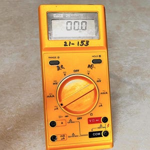 Op de afbeelding: Een gele multimeter met een digitaal display met "00.0". Het apparaat heeft een draaiknop en diverse ingangspoorten. De tekst "21-153" is handgeschreven op het apparaat. Ontworpen voor elektrische metingen.