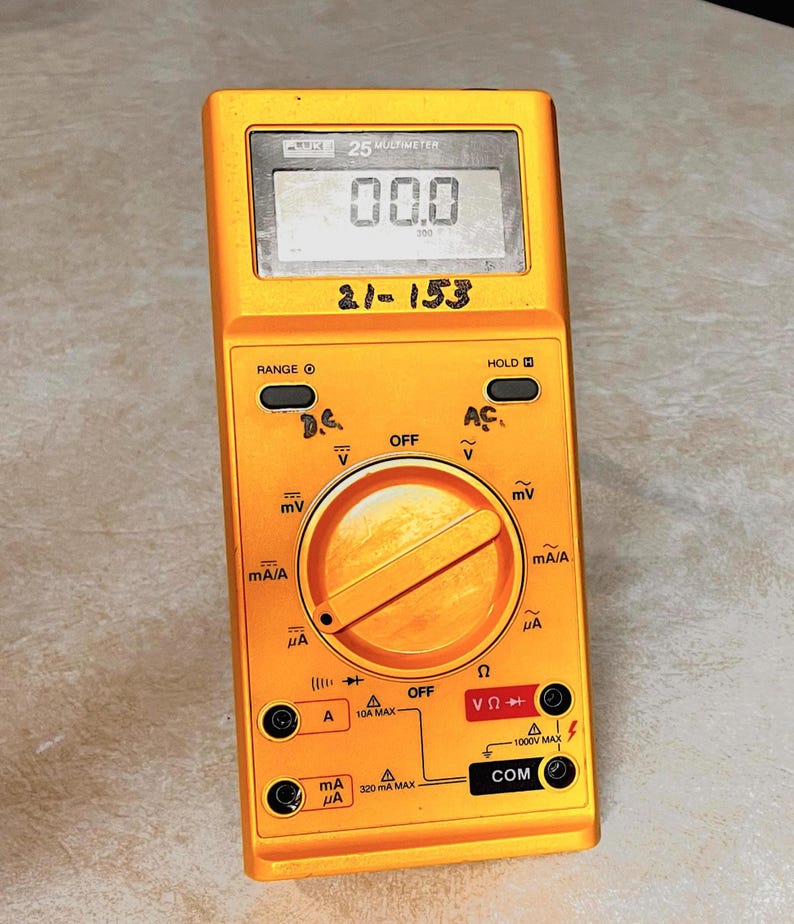 Op de afbeelding: Een gele multimeter met een digitaal display met "00.0". Het apparaat heeft een draaiknop en diverse ingangspoorten. De tekst "21-153" is handgeschreven op het apparaat. Ontworpen voor elektrische metingen.