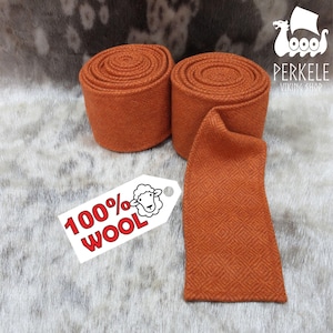 Puede incluir: Dos rollos de tela naranja con un patrón de diamantes y un trozo separado de la misma tela. Una etiqueta dice "100% Lana" con una ilustración de oveja. El logotipo de Perkele Viking Shop está en la esquina superior derecha.