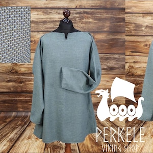 Peut inclure: Une tunique de couleur sarcelle à manches longues, présentée sur un mannequin. La tunique a une encolure simple et une coupe ample. L'image montre également un gros plan de la texture du tissu et le logo Perkele Viking Shop.