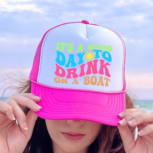 May include: Pink trucker hat with a white mesh back. The hat has a colourful graphic that says "It's a good day to drink on a boat".