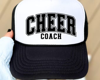 May include: A black and white trucker hat with the words "CHEER COACH" in bold, black, block letters. The hat has a white front panel and a black brim and mesh back. The hat is a classic style, suitable for cheerleading coaches.