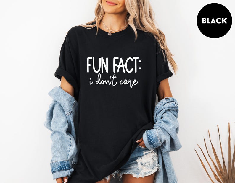 May include: Black t-shirt with the text "FUN FACT: i don't care" in white. The shirt is worn with a denim jacket and shorts. A black circle with the word "BLACK" is in the upper right corner.