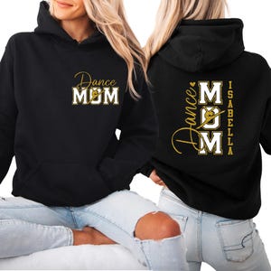May include: Black hoodie with "Dance MOM" in gold script and block letters on the front. The back features "Dance MOM" with a dancer silhouette and the name "Isabella" in gold. A comfortable, casual top for dance mums.