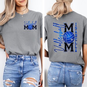 May include: Gray t-shirt with a blue volleyball graphic and the text "Volleyball Mom" on the front. The back of the shirt features the text "Volleyball Mom Isabella" with a volleyball graphic.