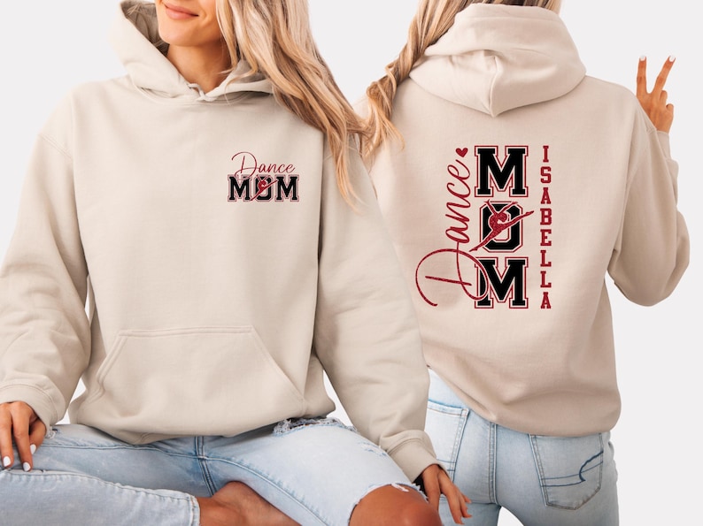 May include: Cream-coloured hoodie with a front pocket and a hood. The front features the text "Dance MOM" in a red and black design. The back of the hoodie displays "Dance MOM" with a dancer graphic, the name "Isabella", and a heart.