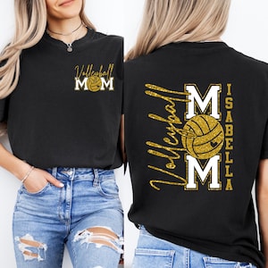 May include: Black t-shirt with gold glitter text and a volleyball graphic. The front of the shirt says "Volleyball Mom" with a volleyball in the center. The back of the shirt has the name "Isabella" and the word "Volleyball" in gold glitter.