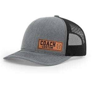 May include: Gray baseball cap with a black mesh back. The cap features a brown leather patch with the words "COACH - CUSTOM" and a baseball graphic.