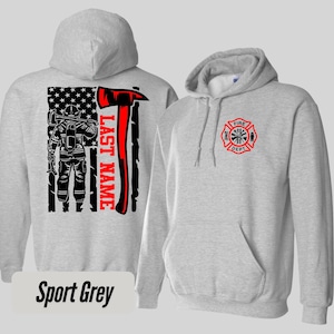 May include: Sport grey hoodie with a firefighter graphic. The back features a firefighter silhouette, an axe, and an American flag design. The front has a fire department emblem.