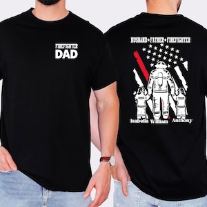 May include: Black t-shirt with the words "FIREFIGHTER DAD" in white on the front. The back features a firefighter graphic with the American flag and the words "HUSBAND * FATHER * FIREFIGHTER". Names are printed below the graphic.