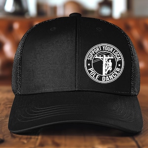May include: Black trucker hat with a white logo that says "Support Your Local Pole Dancer" with a silhouette of a person climbing a utility pole.