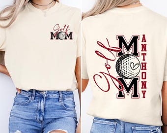 May include: Cream-colored t-shirt with "Golf Mom" and a golf ball graphic on the front. The back features "Golf Mom" in script and the name "Anthony" in a vertical block, also with a golf ball graphic.