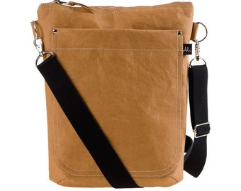 Op de afbeelding: Een bruine, papieren crossbody-tas met een verstelbare zwarte schouderband en een ritssluiting. De tas heeft een groot voorvak met een klep.