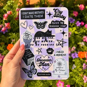 May include: A rectangular sticker sheet with a light purple and white checkered background featuring various black and white illustrations and text including "I don't make mistakes I date them," "Cry Baby," "fueled by feminine rage," and "Decenter Men."