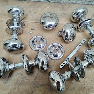 May include: A set of ten chrome door knobs with round, polished handles and various styles of backplates. The knobs are arranged on a wooden surface.