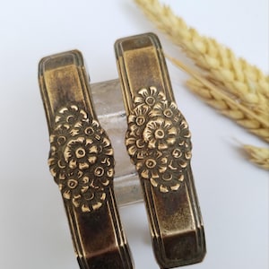 May include: Two antique brass napkin rings with a floral design. The rings are ornate and have a vintage look.