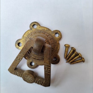 May include: Vintage brass drawer pull with a triangular handle and decorative backplate. Includes five brass screws for installation. The pull has a weathered, vintage appearance, suggesting it is an older piece of hardware.