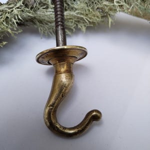 May include: Antique brass hook with a screw thread and a decorative base. The hook is made of solid brass and has a worn, aged finish.