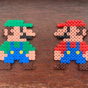 Op de afbeelding: Twee pixel art-figuren gemaakt van kleurrijke kralen. Het personage links is groen, bruin en blauw en lijkt op Luigi uit de Super Mario Bros. videogame-serie. Het personage rechts is rood, bruin en blauw en lijkt op Mario uit de Super Mario Bros. videogame-serie.