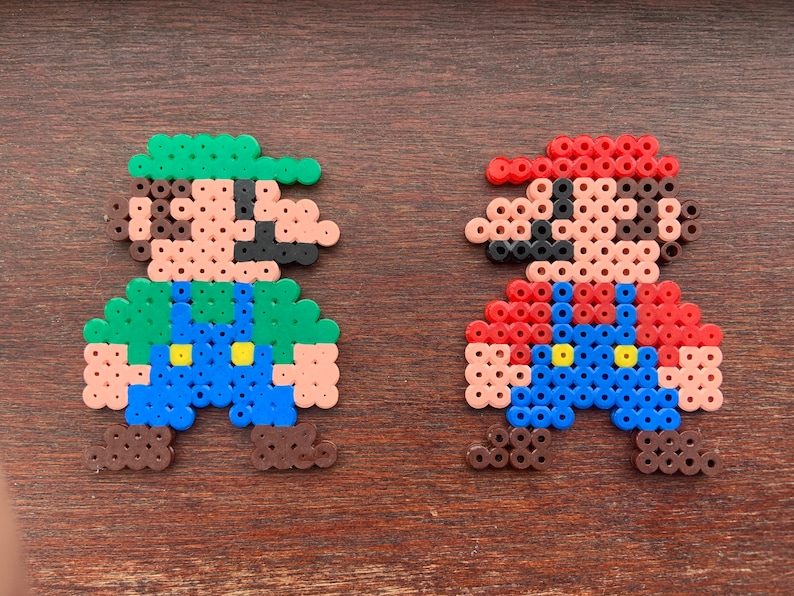 Op de afbeelding: Twee pixel art-figuren gemaakt van kleurrijke kralen. Het personage links is groen, bruin en blauw en lijkt op Luigi uit de Super Mario Bros. videogame-serie. Het personage rechts is rood, bruin en blauw en lijkt op Mario uit de Super Mario Bros. videogame-serie.
