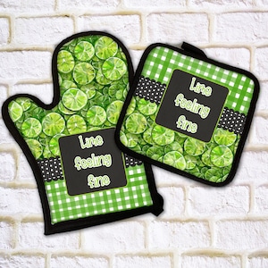 May include: A lime-themed oven mitt and pot holder set. The mitt and pot holder feature a pattern of lime slices and a green and white gingham pattern. The text "Lime feeling fine" is displayed on a black chalkboard-style label.