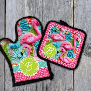 Puede incluir: Conjunto de manopla para horno y posavasos de flamenco rosa con un monograma verde "B" en la manopla. El conjunto presenta un diseño tropical con flamencos rosas, hojas de palmera azules y verdes y flores rosas.