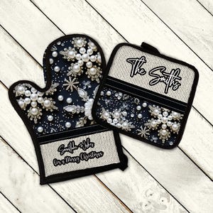 Könnte beinhalten: Ein Set aus zwei schwarzen und weißen Ofenhandschuhen mit einem Schneeflocken- und Perlmuster. Die größere Handschuh hat den Text "Snowflake Wishes for a Merry Christmas" und die kleinere Handschuh hat den Text "The Smiths".