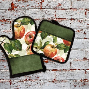 May include: A set of two green oven mitts with a white background and a watercolor design of red apples and green leaves.