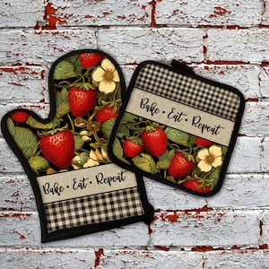 May include: A set of two black and white checkered oven mitts with a strawberry and floral design. The mitts have the text "Bake. Eat. Repeat" on them.