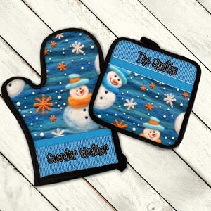 May include: A blue oven mitt and pot holder set with a snowman design. The mitt and pot holder feature a blue background with snowflakes, orange stars, and snowmen wearing hats and scarves. The text "Sweater Weather" is on the mitt, and "The Smiths" is on the pot holder.