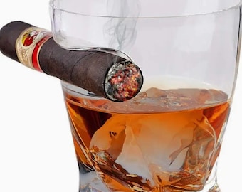 May include: A clear, angled whiskey glass with amber liquid and a large ice cube. A lit cigar rests on the glass's rim, with smoke rising. The cigar has a red and gold band.