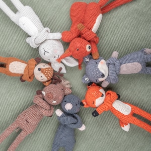 Op de afbeelding: Een groep van zeven gehaakte knuffels in verschillende kleuren en dierlijke vormen, waaronder een vos, een hert, een konijn, een wolf, een beer en twee andere dieren. De dieren zijn in een cirkel op een groene stoffen achtergrond gerangschikt.