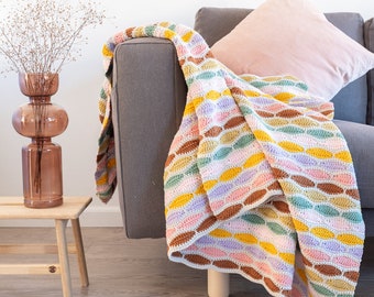 May include: A colorful crocheted throw blanket with a wavy pattern in shades of pink, yellow, brown, and green. The blanket is draped over a gray couch.
