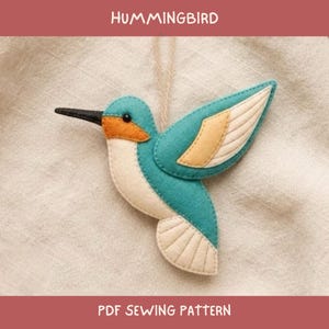 Puede incluir: Un adorno de fieltro con forma de colibrí que presenta secciones en color verde azulado, crema y naranja, con un pico negro y un cordel. El texto HUMMINGBIRD y PDF SEWING PATTERN es visible arriba y abajo, indicando un proyecto de costura.